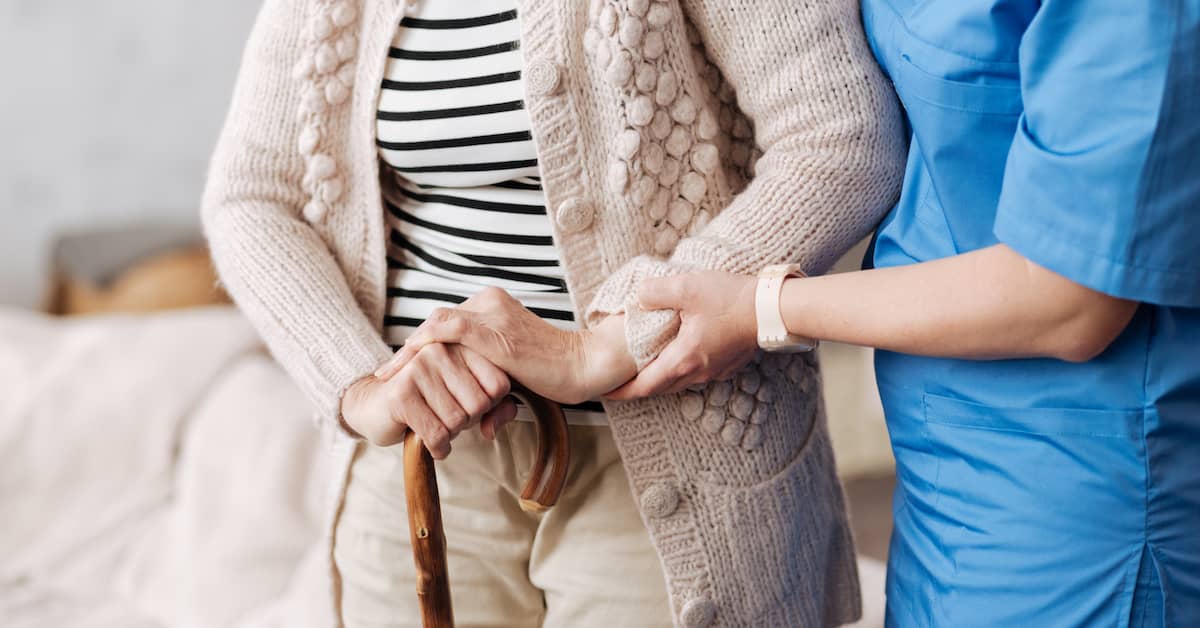 a nurse helps an old woman holding a cane | Boller and Vaughan